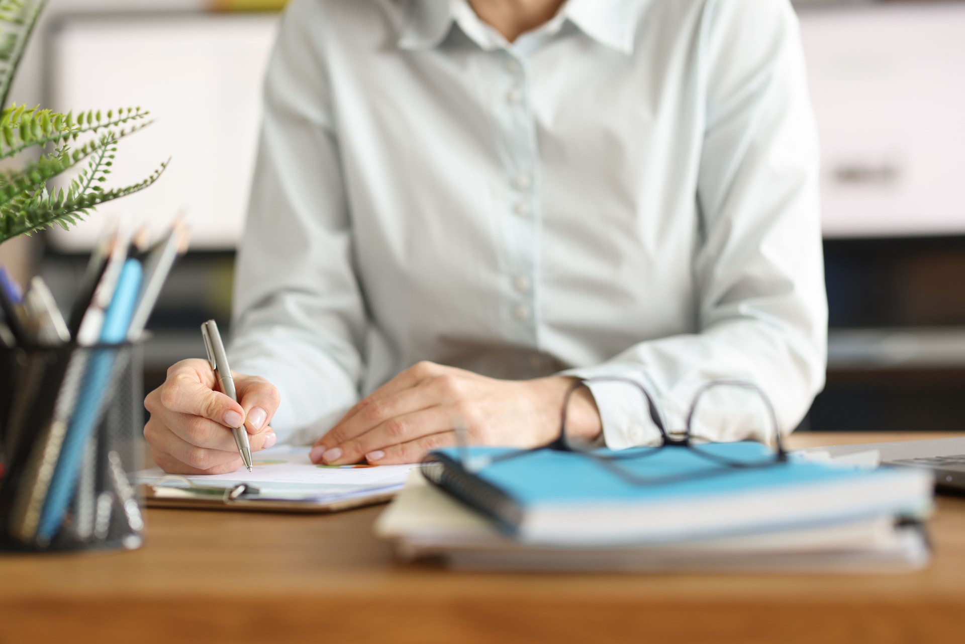 Woman writes with pen in documents at workplace